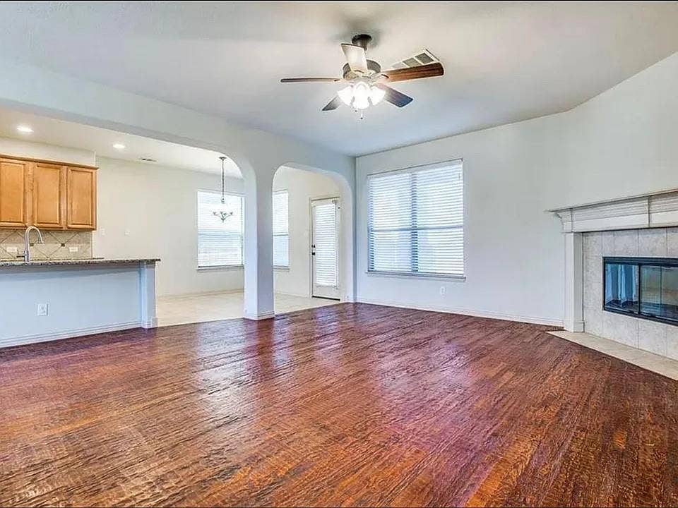 13990 Stevens Point Drive, Frisco, TX 75033 Spacious living area featuring wood-finish flooring, a ceiling fan with integrated lighting, and a fireplace with a mantel and tile surround