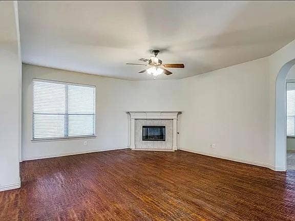 13990 Stevens Point Drive, Frisco, TX 75033 Spacious living area featuring rich wood-finish flooring, a contemporary fireplace with a decorative mantel, and a ceiling fan with light fixture