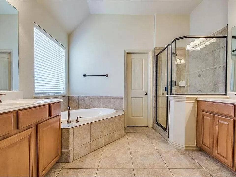 13990 Stevens Point Drive, Frisco, TX 75033 Bathroom featuring a corner soaking tub with tiled surround, a separate shower with a glass enclosure, dual vanity sinks with light wood cabinetry and countertops, and tiled flooring