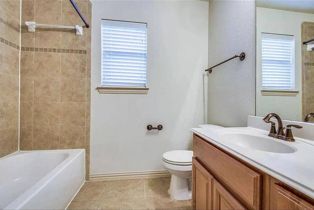 13990 Stevens Point Drive, Frisco, TX 75033 Bathroom featuring a white bathtub, floor-to-ceiling tiled shower surround with accent band, single window with blinds, and a vanity with an integrated sink and bronze-finish faucet