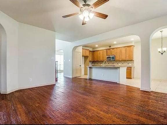 13990 Stevens Point Drive, Frisco, TX 75033 Spacious interior with wood-finish flooring, arched doorways, a ceiling fan, and an integrated kitchen featuring wood cabinetry, stainless steel appliances, and a breakfast bar with a stone-look countertop