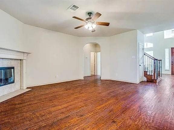 13990 Stevens Point Drive, Frisco, TX 75033 Spacious living area featuring wood-finish flooring, a tiled fireplace with a white mantel, and an arched doorway
