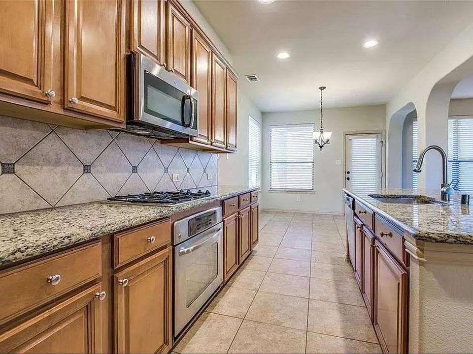 13990 Stevens Point Drive, Frisco, TX 75033 Kitchen featuring wood cabinetry, granite countertops, tile flooring, and stainless steel appliances including a built-in oven and microwave