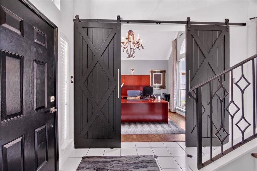 4243 Millview Lane, Dallas, TX 75287 Foyer with view of home office with elegant sliding wood doors. Staircase black balusters and designer light fixture blend sophistication and warmth to welcome guests.