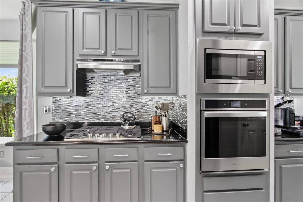 4243 Millview Lane, Dallas, TX 75287 View of gas range with outside vented hood. Sleek, modern glass backsplash is easy to clean. Built in microwave and oven. New Oven 2019. New Whirlpool cooktop added in 2025