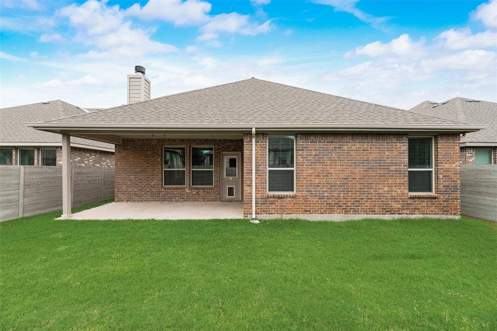 Back of house with brick siding, a shingled roof, a fenced backyard, and a patio area