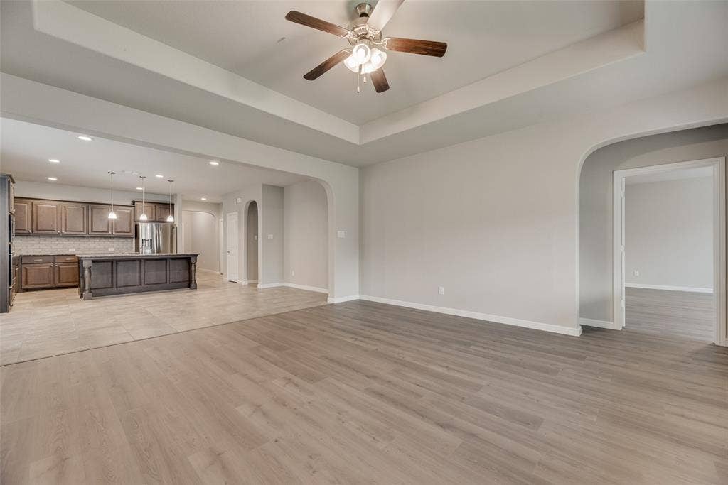 Unfurnished living room featuring arched walkways, ceiling fan, recessed lighting, light wood-style flooring, and a tray ceiling