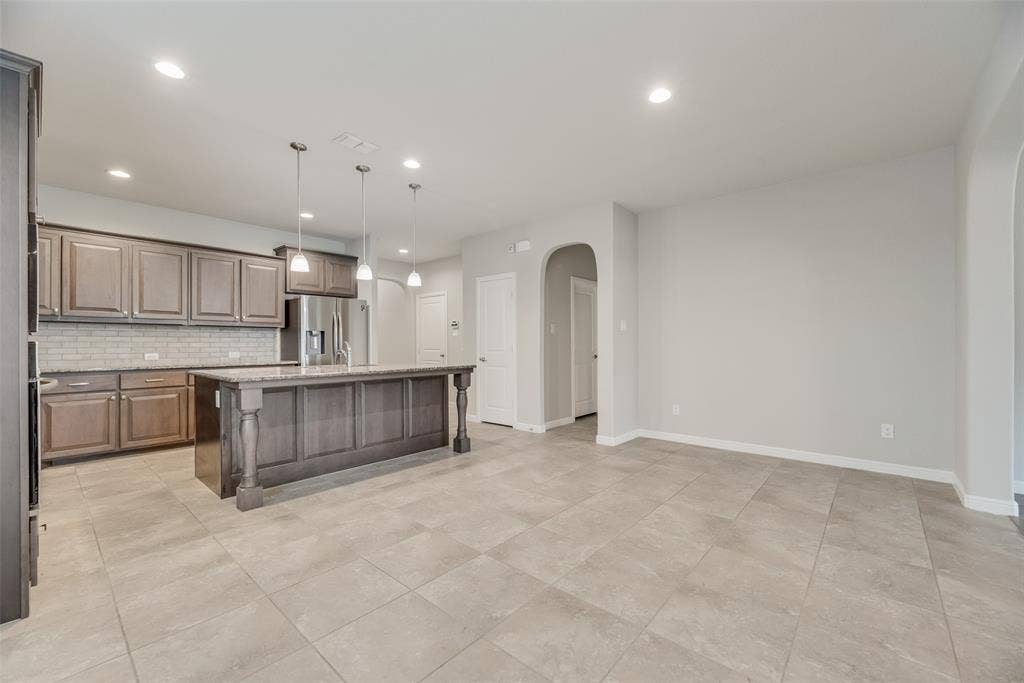 Kitchen featuring stainless steel fridge with ice dispenser, arched walkways, decorative backsplash, recessed lighting, and a center island with sink