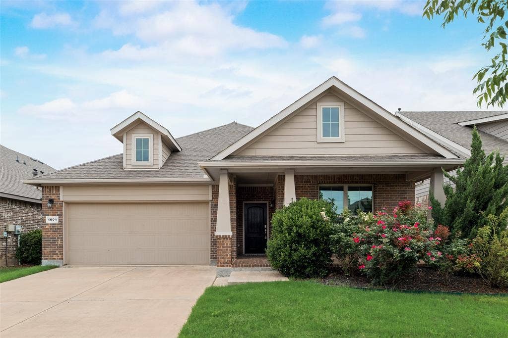 View of front of property with brick siding, driveway, an attached garage, a shingled roof, and a front lawn