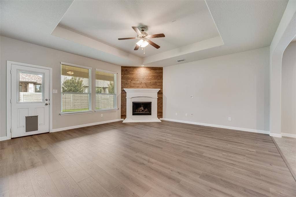 Unfurnished living room featuring a raised ceiling, a ceiling fan, a fireplace with raised hearth, light wood-style floors, and arched walkways