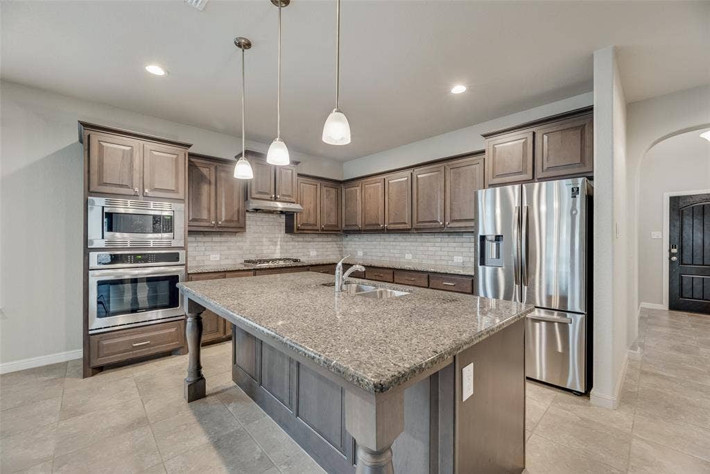 Kitchen featuring appliances with stainless steel finishes, under cabinet range hood, arched walkways, decorative backsplash, and recessed lighting