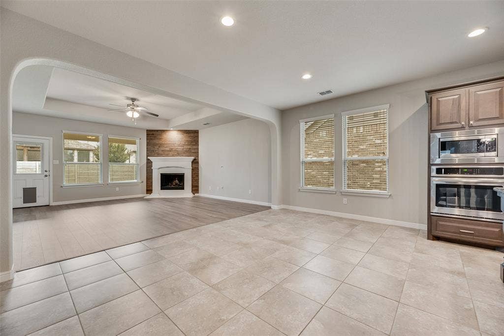 Unfurnished living room featuring light tile patterned floors, ceiling fan, recessed lighting, a raised ceiling, and a large fireplace