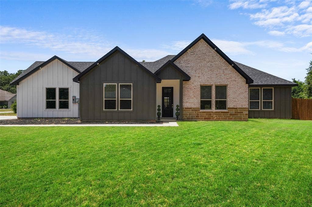 609 Luzon Street, Tool, TX 75143 Contemporary exterior featuring a brick facade with stone detailing, dark siding, white board and batten accents, a black shingle roof, and a dark front door