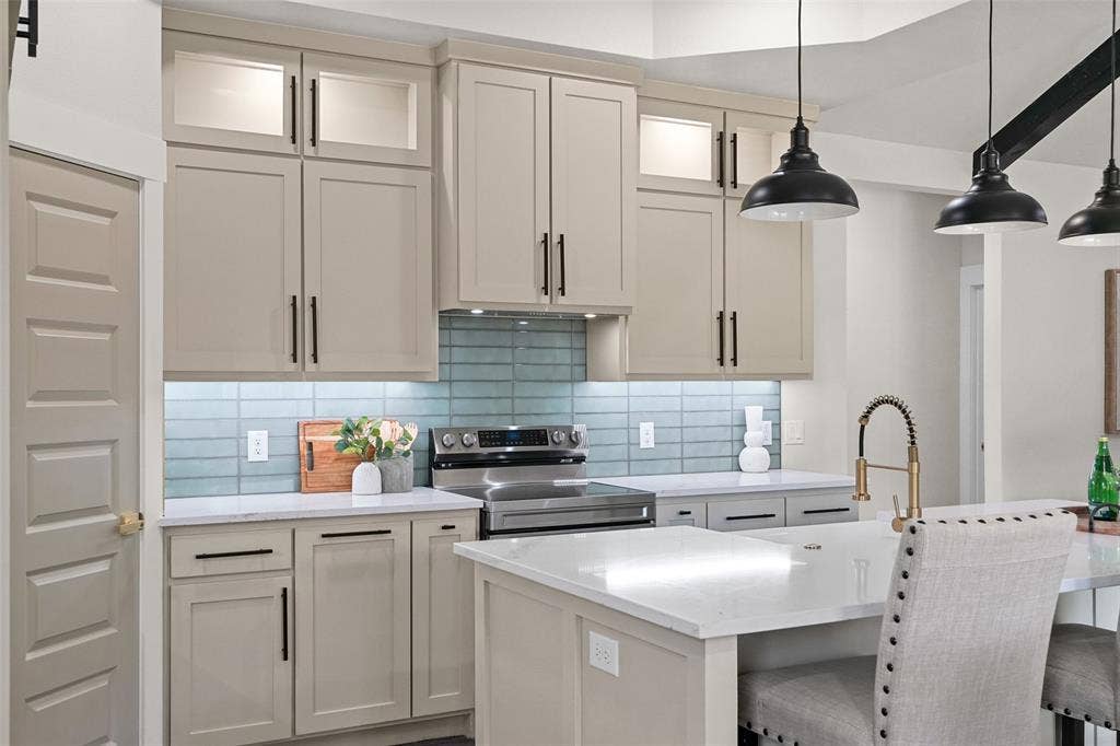609 Luzon Street, Tool, TX 75143 Modern kitchen featuring light cabinetry with black hardware, a blue tile backsplash, stainless steel range, and a kitchen island with a gold-tone faucet