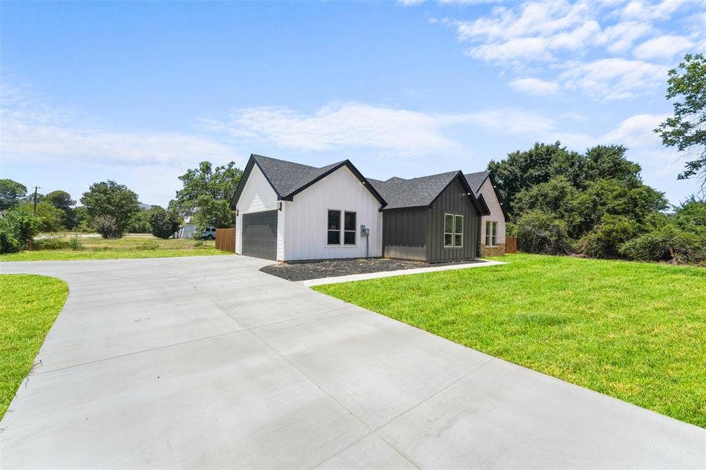 609 Luzon Street, Tool, TX 75143 Modern farmhouse exterior featuring white vertical siding, dark gray board and batten accents, a black shingled roof, a concrete driveway, and a manicured lawn