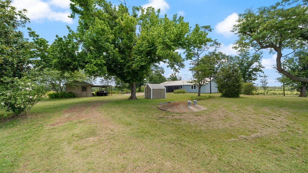 1053 Vz County Road 4206, Athens, TX 75752 Expansive grassy yard area featuring mature trees, a wooden shed with an attached covered structure, a metal utility shed, and a light-colored property in the background