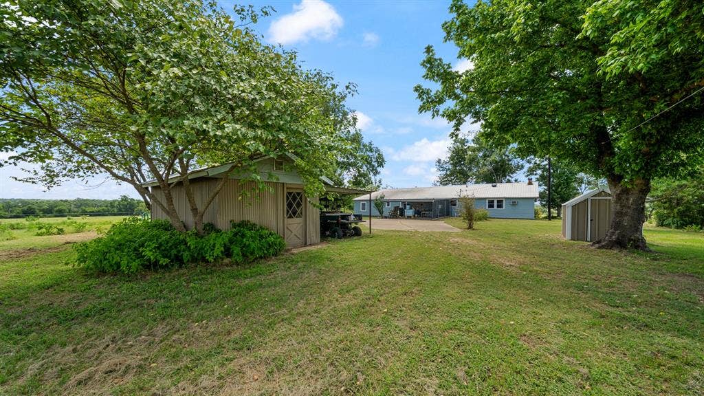 1053 Vz County Road 4206, Athens, TX 75752 Expansive green lawn featuring mature trees, a detached storage shed with a diamond-pane window, and a secondary metal storage shed