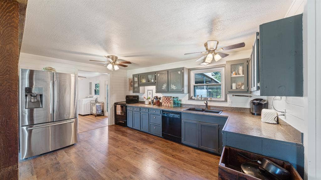 1053 Vz County Road 4206, Athens, TX 75752 Open-concept kitchen featuring wood-finish flooring, stainless steel refrigerator, dark cabinetry with some glass-front uppers, and ceiling fans with light fixtures