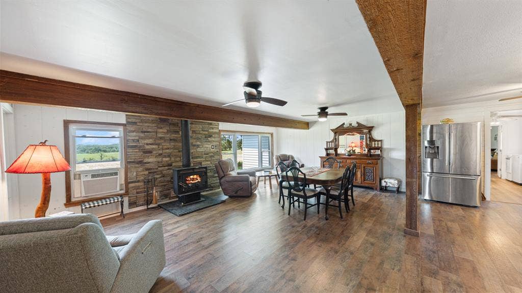 1053 Vz County Road 4206, Athens, TX 75752 Open-concept interior featuring wood-finish flooring, exposed wood ceiling beams, a stone accent wall, and a built-in wood-burning stove