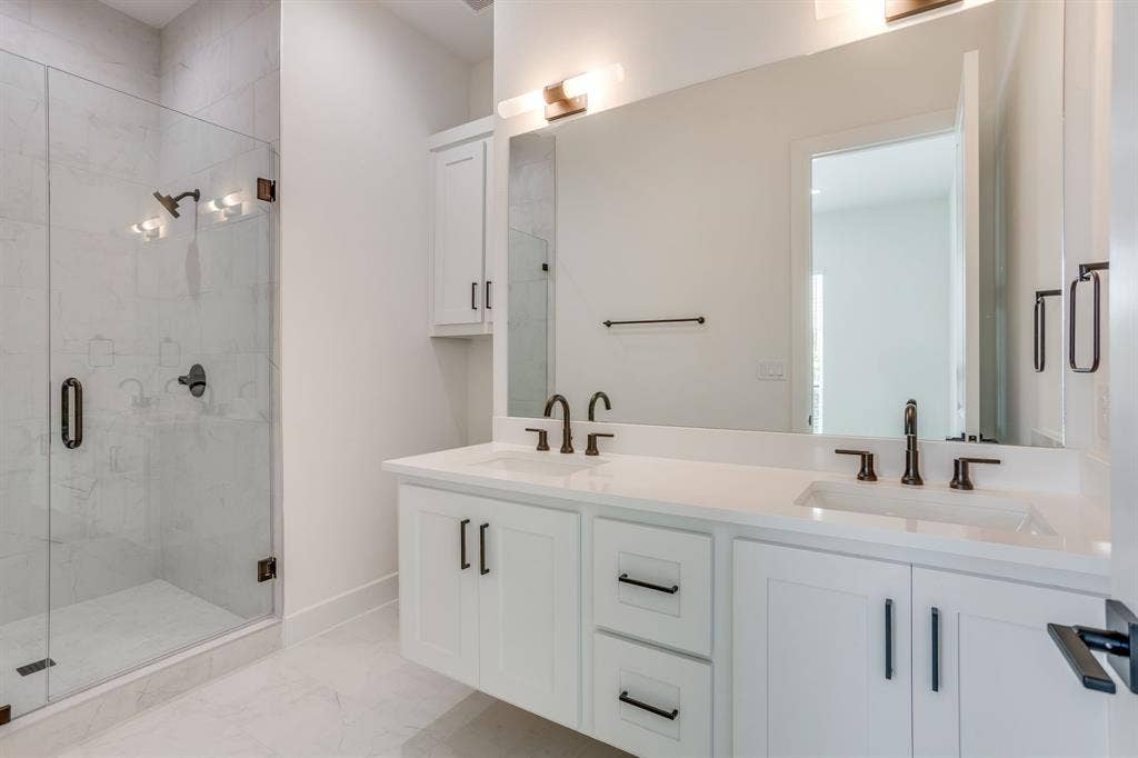 123 Thornton Street, Arlington, TX 76013 Contemporary bathroom featuring a spacious glass-enclosed shower with a multi-light fixture, dual vanity with white cabinetry and integrated sinks, a large wall-mounted mirror, and dark bronze fixtures