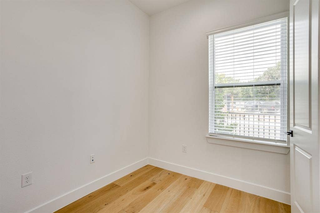 123 Thornton Street, Arlington, TX 76013 Bright room featuring a large window with horizontal blinds, light wood-finish flooring, white baseboards, and a white paneled door