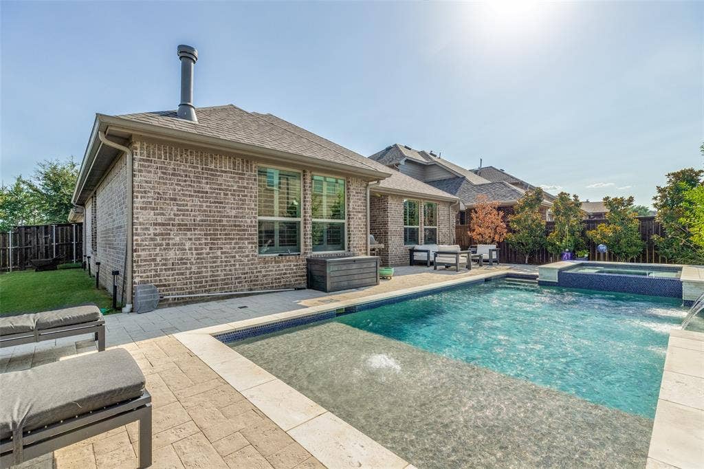Backyard featuring a rectangular swimming pool with integrated spa, paver patio, brick exterior, and a privacy fence