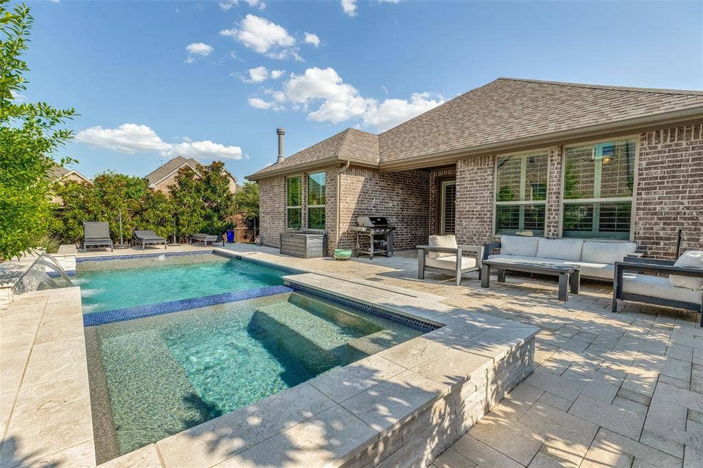 Expansive backyard featuring a built-in swimming pool with an integrated spa, a paver patio, brick exterior, and large windows with interior shutters
