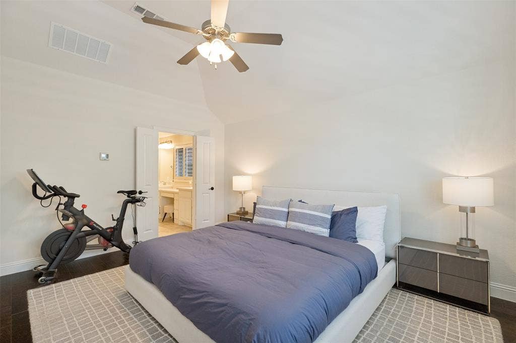 Bedroom featuring vaulted ceilings, ceiling fan with integrated lighting, wood-finish flooring, and an en-suite bathroom with a vanity and mirror