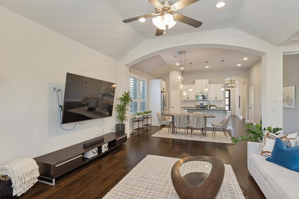 Living area with vaulted ceilings, dark wood-finish flooring, and an arched entry leading to the dining area and kitchen