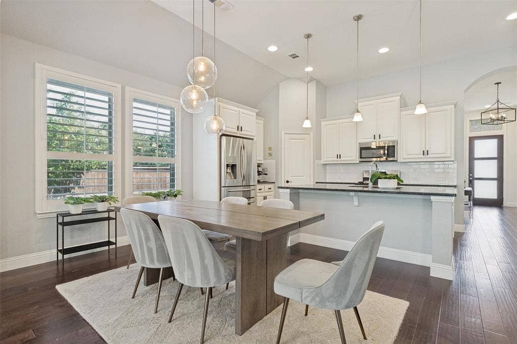 Open-concept dining area featuring dark wood-finish flooring, white plantation shutters, and a modern chandelier