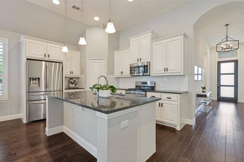 Modern kitchen featuring a central island with a dark stone countertop, white shaker-style cabinetry, stainless steel appliances, and wood-finish flooring