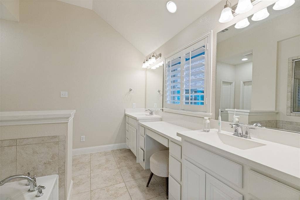Spacious bathroom featuring dual vanities with integrated sinks, white cabinetry, and light-toned countertops