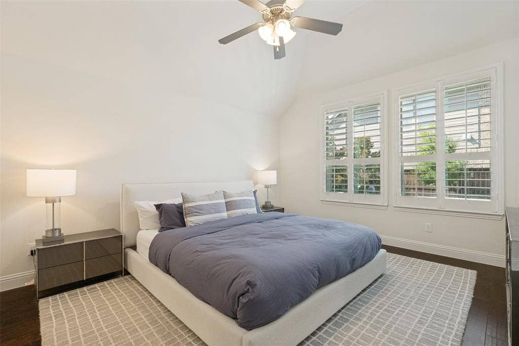 Bedroom featuring a vaulted ceiling with a ceiling fan, dark wood-finish flooring, and white plantation shutters on multiple windows