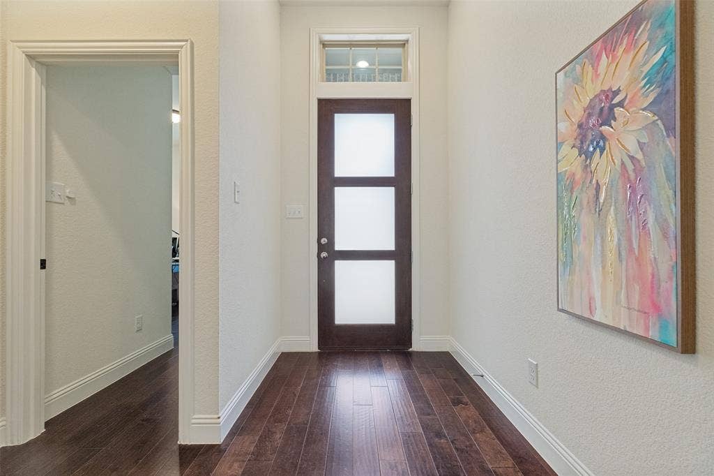 Entryway featuring rich wood-finish flooring, a dark-stained door with frosted glass panels, an overhead transom window, white baseboards, and a framed doorway
