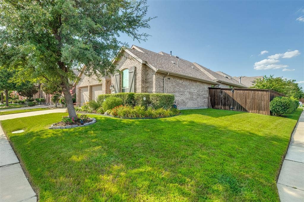 Brick exterior residence with a side-facing garage, mature tree, established landscaping, and wooden privacy fencing
