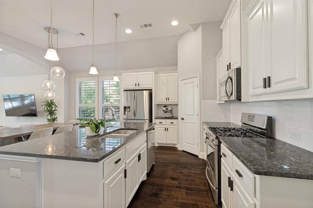 Kitchen featuring dark wood-finish flooring, white cabinetry with dark hardware, stainless steel appliances, and dark speckled countertops