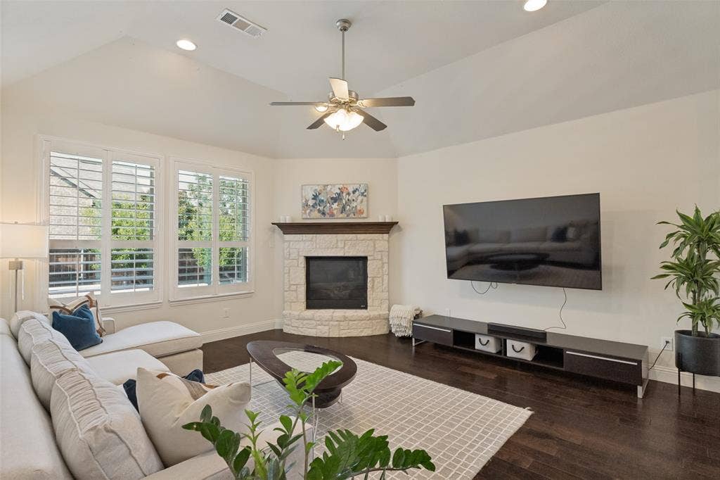 Living area featuring a vaulted ceiling, wood-finish flooring, and two windows with white plantation shutters