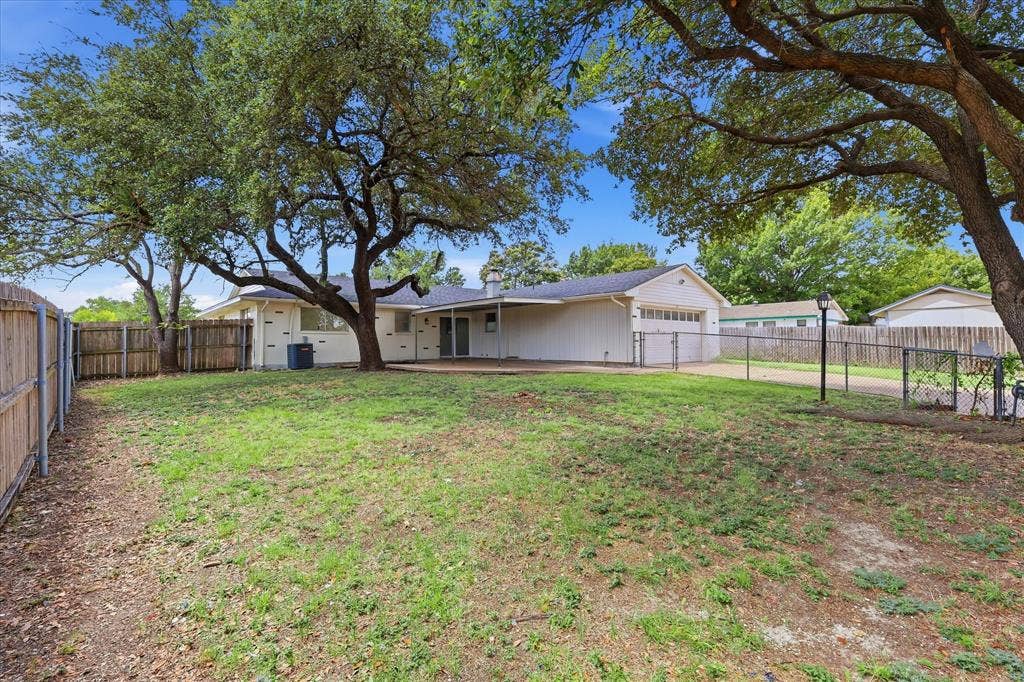 3301 Hillsdale Lane, Garland, TX 75042 Expansive backyard featuring mature trees, a wooden privacy fence, chain-link fencing, and a concrete patio