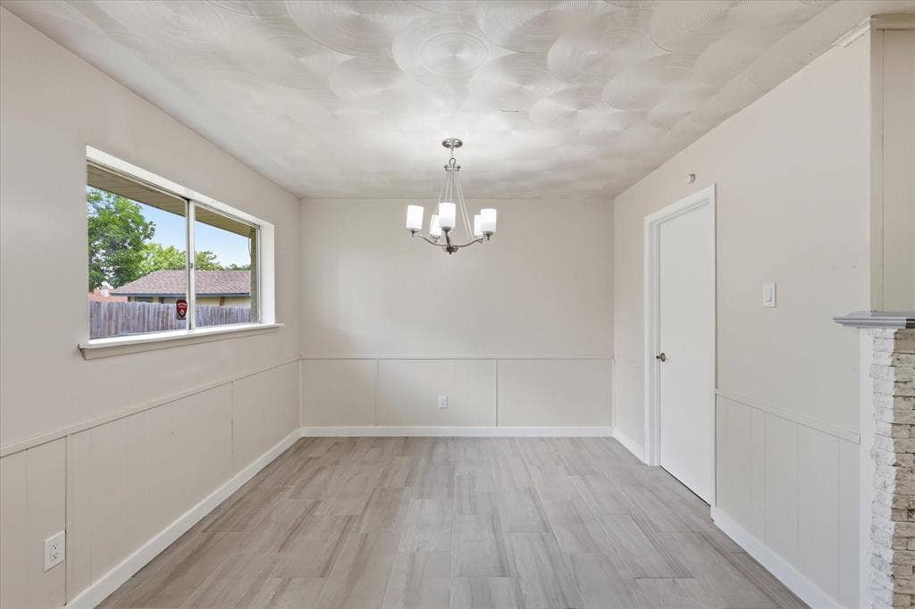 3301 Hillsdale Lane, Garland, TX 75042 Spacious room featuring wood-finish flooring, wainscoting, and a multi-light chandelier