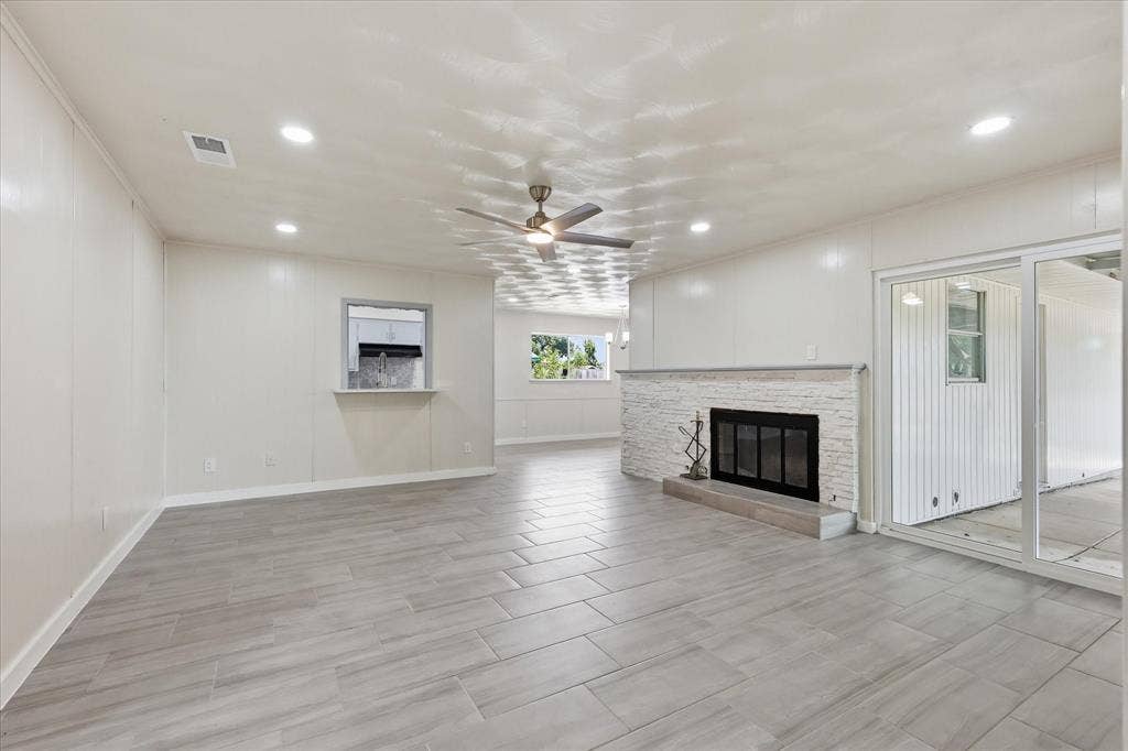 3301 Hillsdale Lane, Garland, TX 75042 Spacious living area featuring light wood-finish flooring, a white brick fireplace with a dark firebox, a ceiling fan, recessed lighting, and a pass-through window with a lower shelf