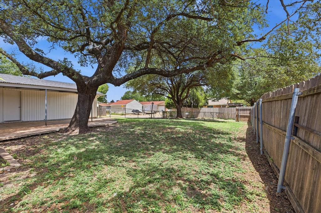 3301 Hillsdale Lane, Garland, TX 75042 Spacious backyard featuring a prominent mature tree, natural grass, and a wood privacy fence