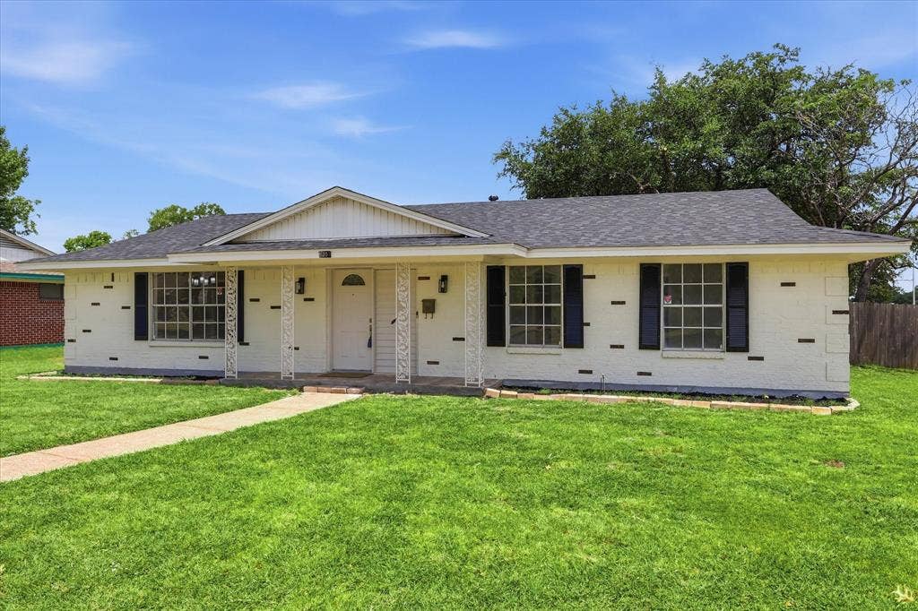 3301 Hillsdale Lane, Garland, TX 75042 Single-story residence featuring a white brick exterior with dark trim accents, a front porch with decorative columns, a gabled entry, and a dark shingle roof