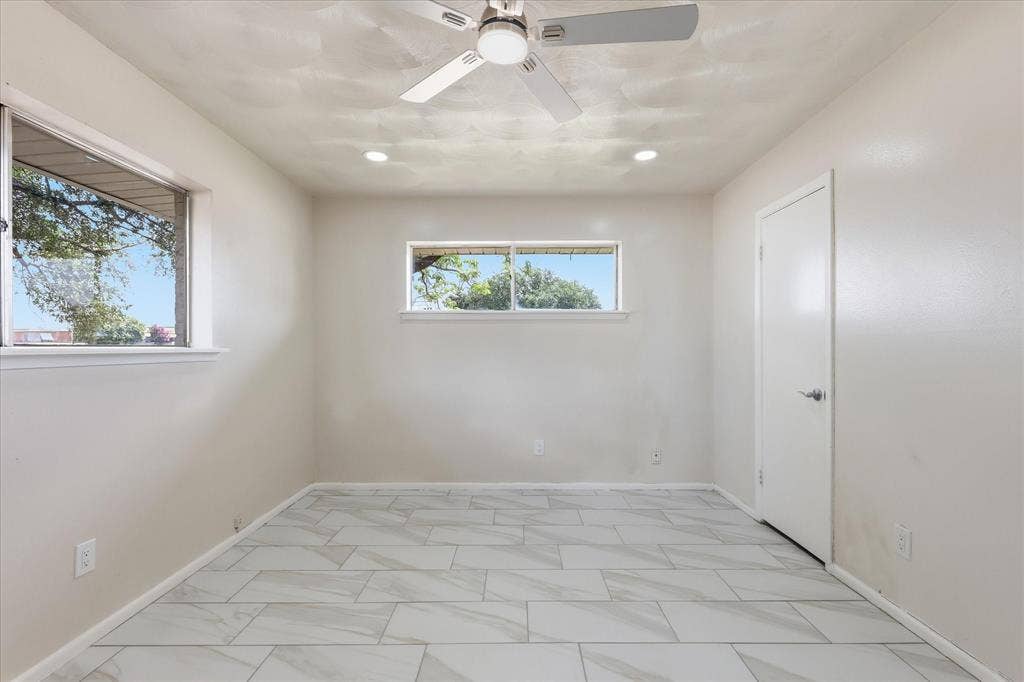 3301 Hillsdale Lane, Garland, TX 75042 Spacious room featuring large format tile flooring, two windows, recessed lighting, a ceiling fan, and a solid door