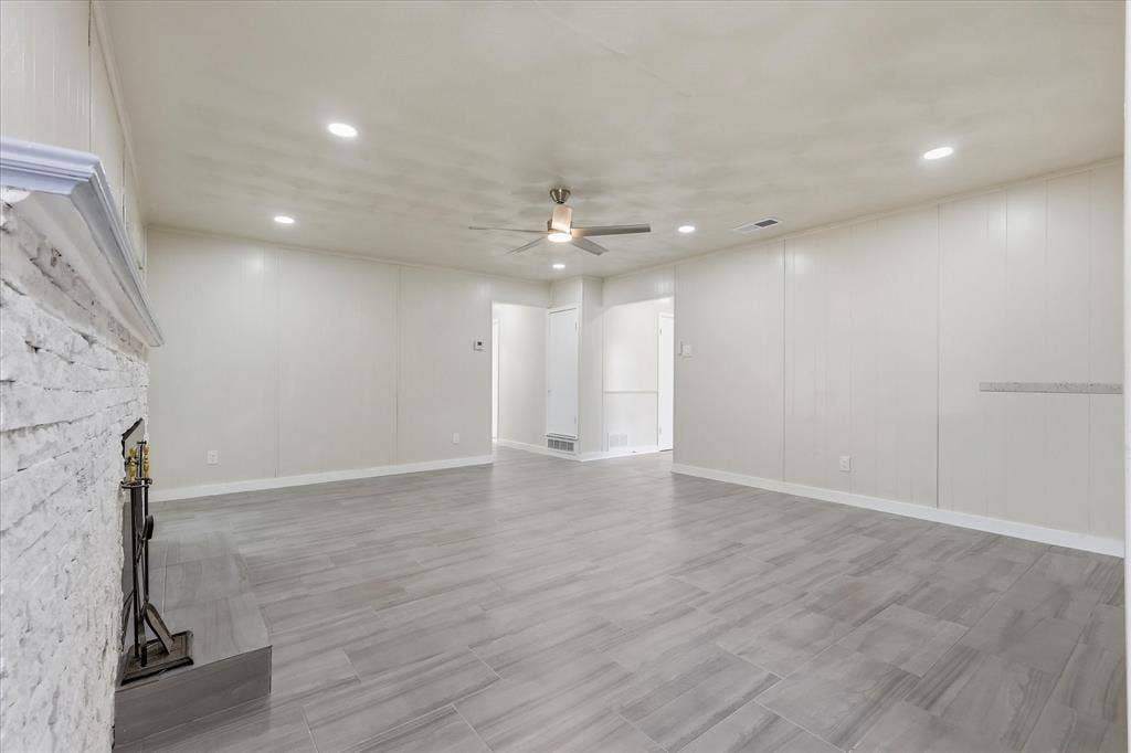3301 Hillsdale Lane, Garland, TX 75042 Spacious living area featuring a stacked stone fireplace with mantle, wood-finish tile flooring, recessed lighting, and a ceiling fan