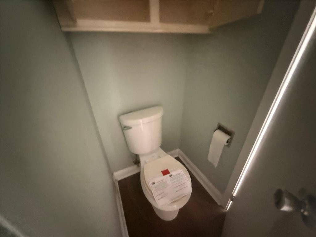 209 Lone Star Road, Trinidad, TX 75163 Powder room featuring a white toilet, wood-finish flooring, light blue wall paint, and built-in upper cabinetry