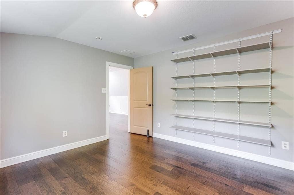Room featuring wood-finish flooring, light grey walls, and extensive built-in shelving