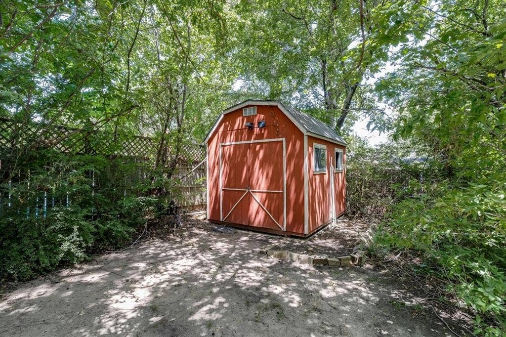 Freestanding red storage shed featuring a gable roof, double barn doors, and two windows