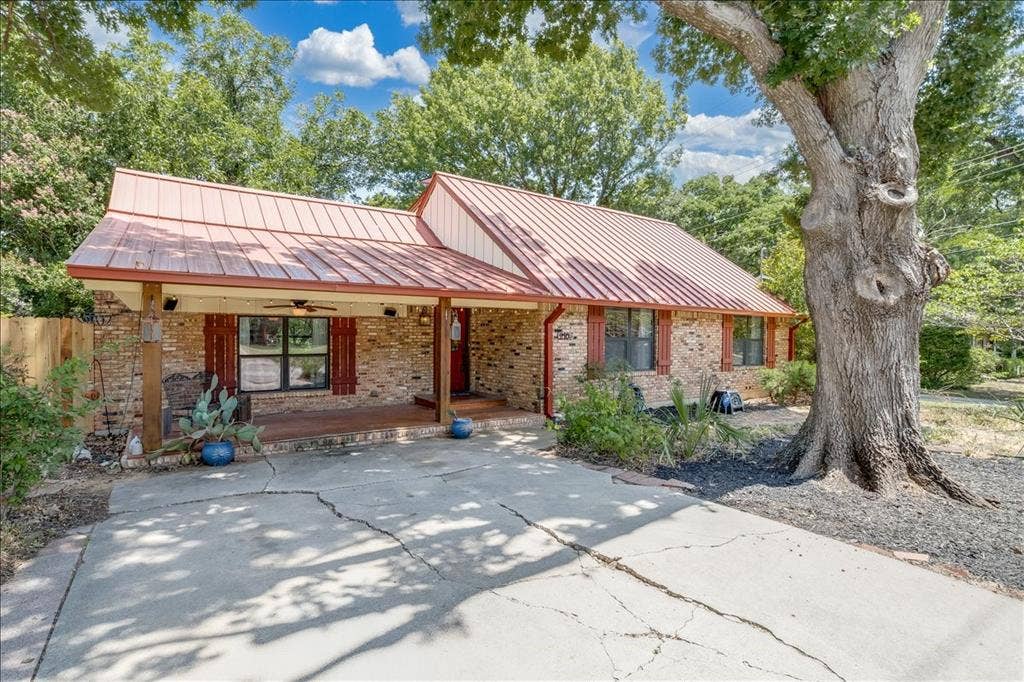 Brick exterior with a standing seam metal roof, covered front porch, and mature trees