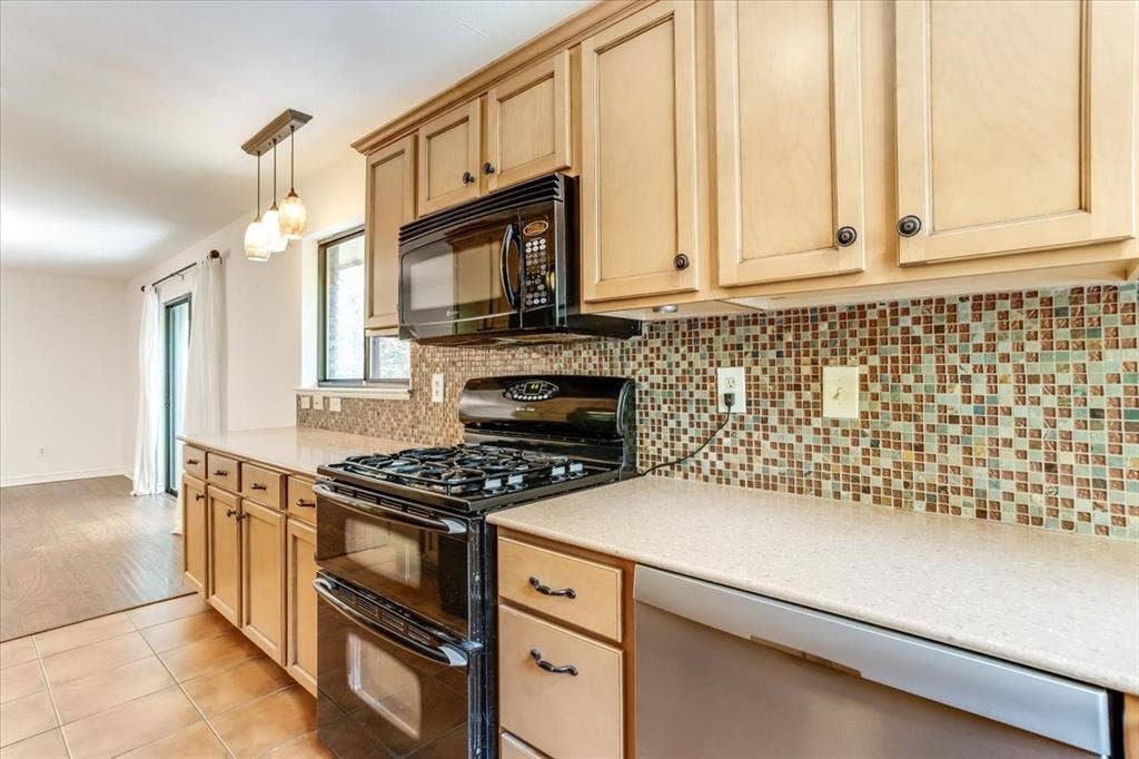Kitchen featuring light wood cabinetry, a mosaic tile backsplash, black gas range with a double oven, black built-in microwave, and a counter-depth dishwasher