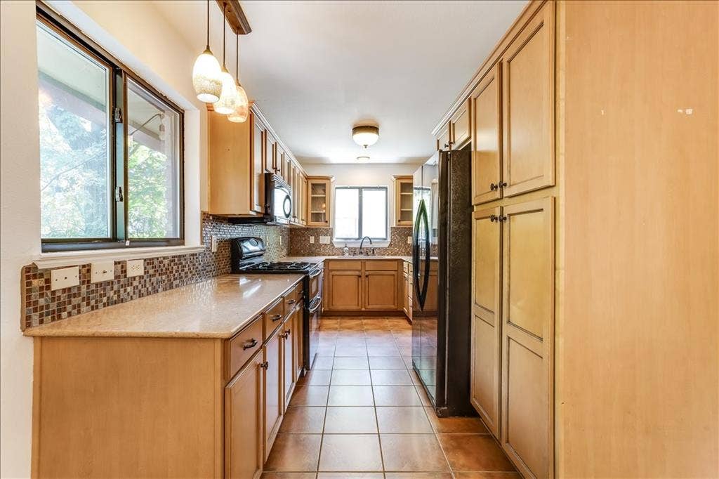 Galley kitchen with light wood-finish cabinetry, tile flooring, and granite-style countertops